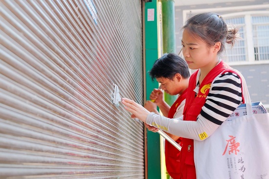 湘龙街道湘润社区志愿者何凌志、网格员周满意正手持铲子、刮刀，奋力清理墙上的小广告。章帝 摄