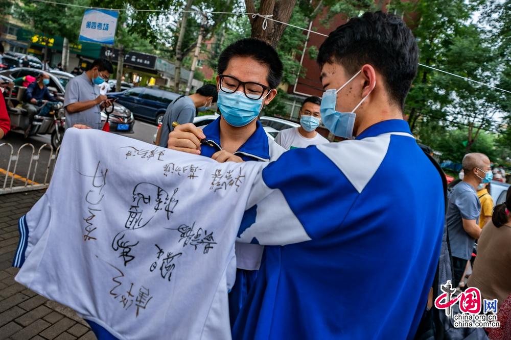 7月10日,北京中关村中学考点外,结束考试的考生在同学校服上签名留念.