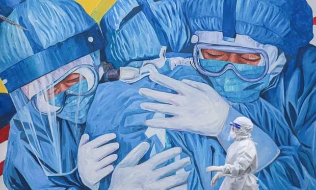 马来西亚,一位身穿防护服的医护人员走过一幅巨大的壁画,壁画上是相拥