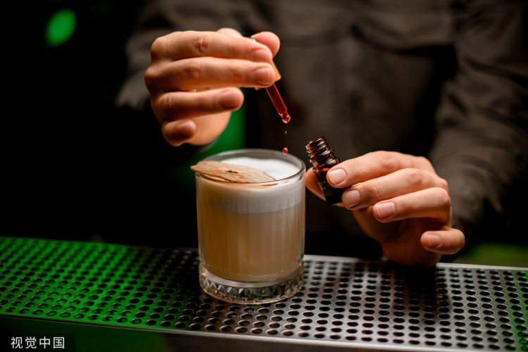 鸡尾酒杯中，调酒师小心地用移液管加入一滴香精。/视觉中国
