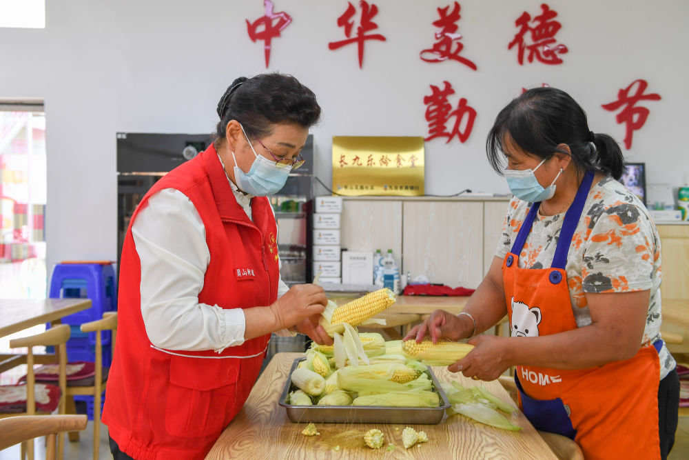 8月24日，在团山街道长山花园社区食堂，吴亚琴（左）与志愿者房桂香一同剥玉米。新华社记者 张楠 摄