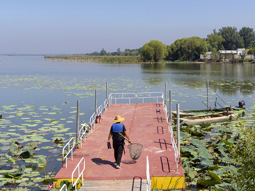 李国忠手持网兜准备驾船去湖区打捞垃圾。（受访者供图）