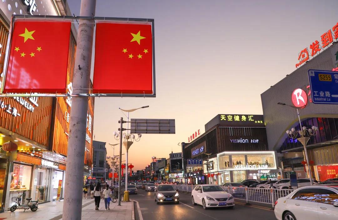 当夜幕降临,鲜艳的国旗在繁华街道的霓虹映衬下,更显现出活力,让整个