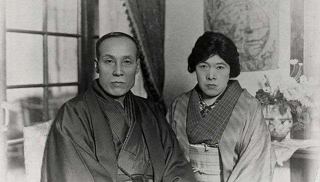 black and white photograph of Yosano Akiko and her husband sitting next to one another in a decorated house