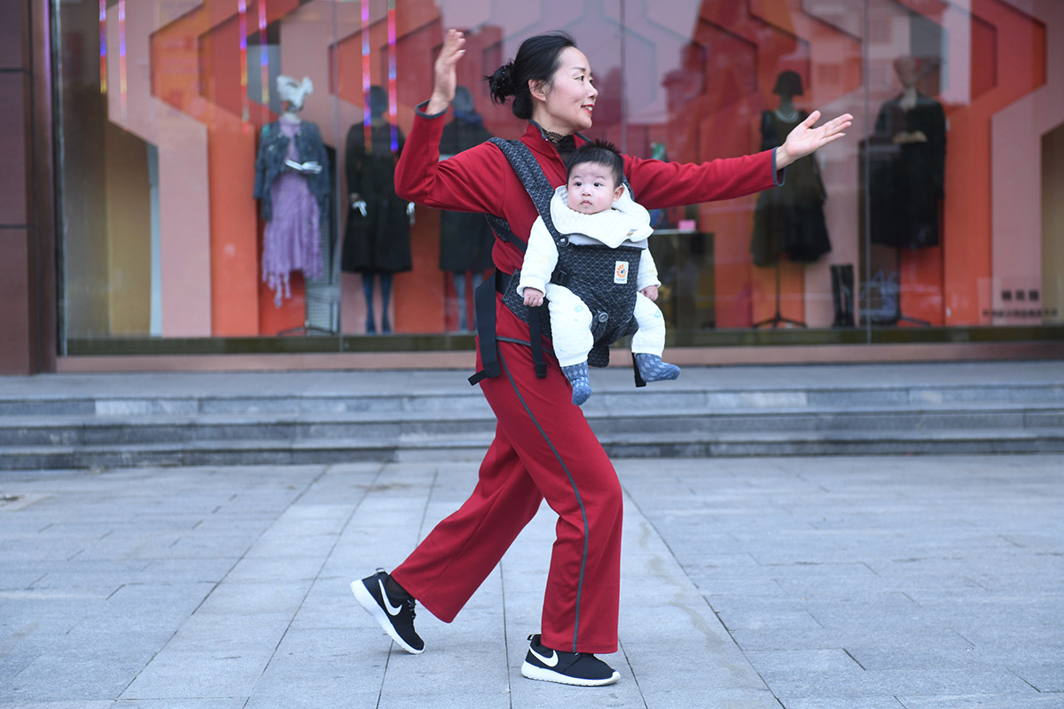 10月19日,安徽省阜阳市颍州区颍西街道办事处振兴社区的“功夫姥姥”姚玲采取“袋鼠抱”的方式怀揣外孙在街头小广场练太极。她怀中的宝宝不哭不闹,眼神随着女子的动作移动。 王彪/人民视觉 图