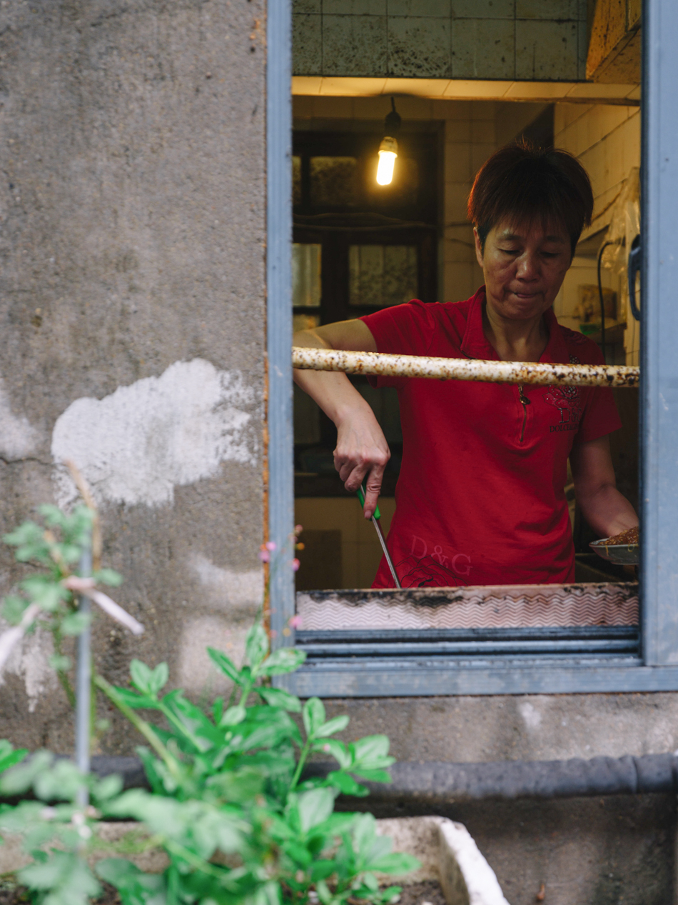 定海港路沿街窗内烧菜的阿姨,这条路原名周家嘴路,街道后边原本有一条河浜,几十年前被填平,已经找不到曾经存在的痕迹。