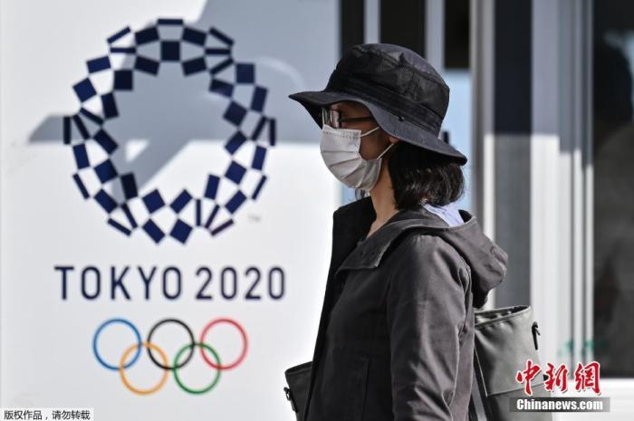资料图:2020年10月21日,东京奥运会和残奥会组织委员会21日在东京向媒体公开了,观众等进入赛场时通过的行李安检区运营的实证试验。奥组委将根据本次的测试结果等,讨论奥运时的对策。图为一名女士走过2020年东京奥运会海报。