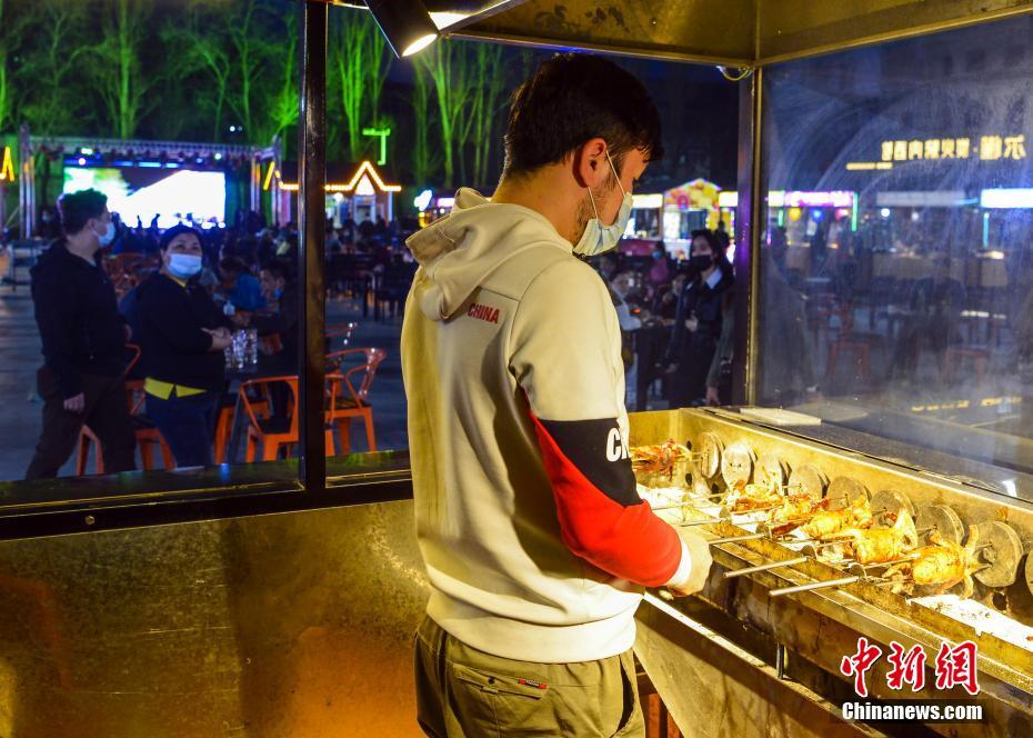 4月10日晚,新疆维吾尔自治区乌鲁木齐市延安路欢乐时光夜市的一位餐饮摊点工作人员在制作餐品。近日,乌鲁木齐的日夜星光、野马、欢乐时光等多个夜市陆续迎客。 中新社记者 刘新 摄