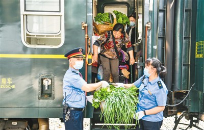 在贵州桐梓站，乘务员帮助乘坐5630次列车卖菜的村民搬运蔬菜下车。