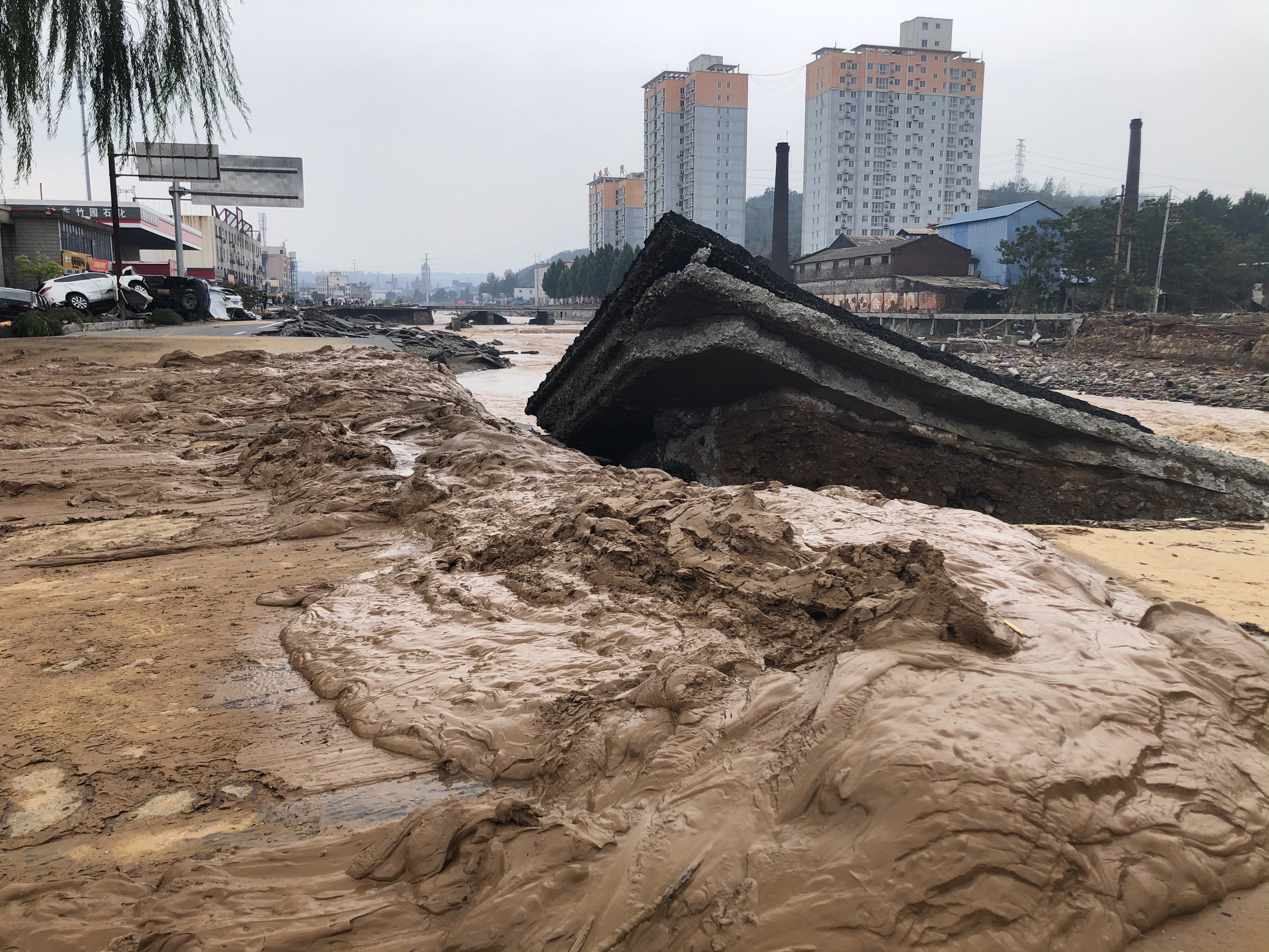 米河镇东竹园村后山上被洪水冲下的泥土，一路直冲进汜水河。图中翘起的板状物为310国道铺装层。澎湃新闻记者 王健