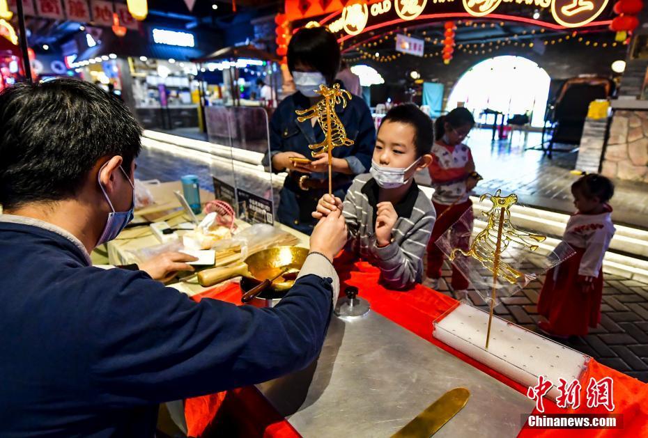  2月7日，新疆乌鲁木齐市城南往事怀旧美食街区，非遗传承人刘孝卿为小朋友制作牛造型的糖画。中新社记者 刘新 摄