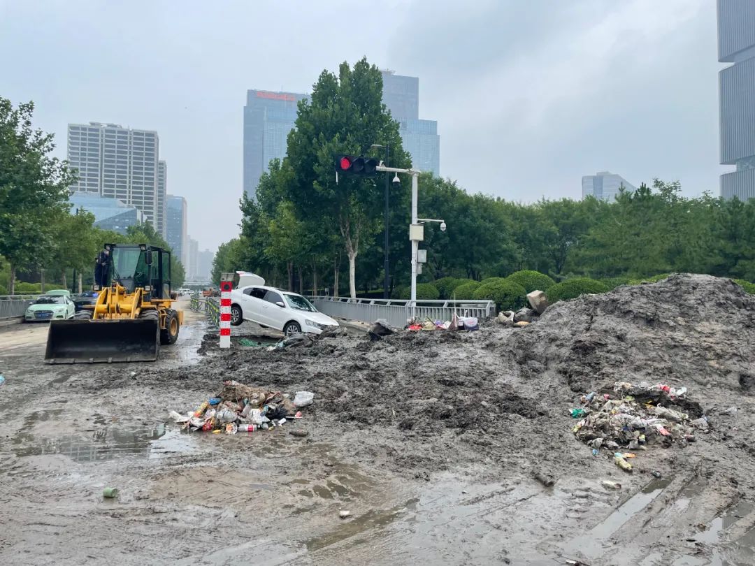 7月23日，事发地南边100米，郑州市普惠路与东站北街十字路口仍有大量淤泥，白色的轿车悬空在自行车道的护栏上。新京报记者 涂重航 摄