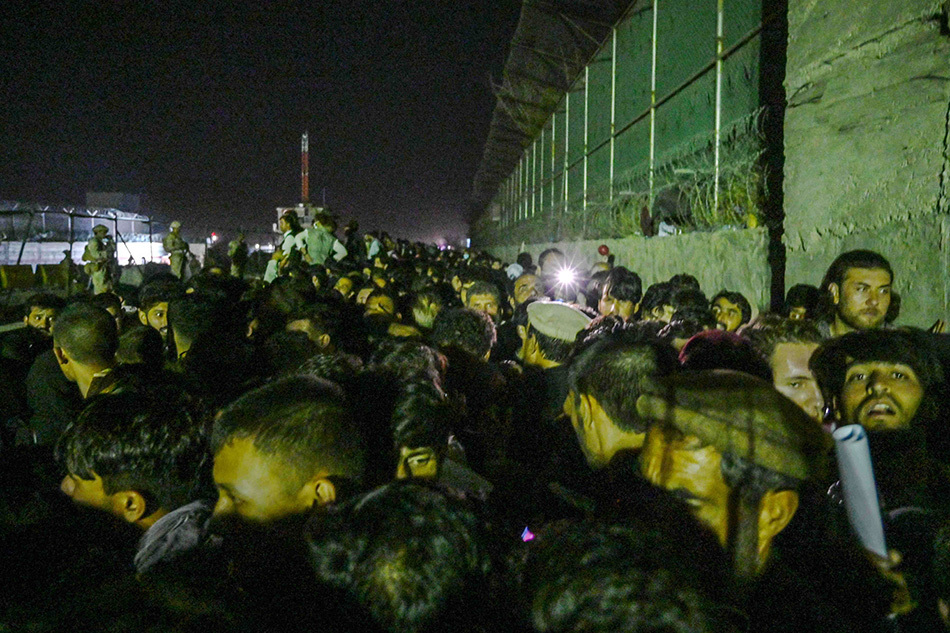 而围墙另一边，阿富汗人在机场外等待。