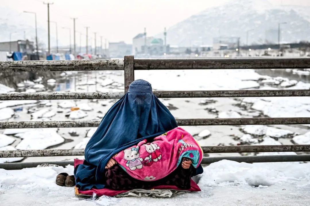 ▲ 2022年1月6日，喀布尔一座积雪覆盖的桥上，一名身穿罩袍的阿富汗妇女和她的孩子向路人寻求施舍。