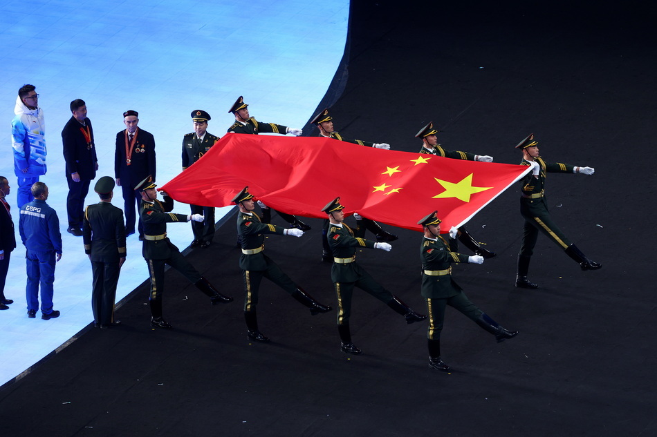 2022年2月4日，北京冬奥会开幕式现场，8名中国军人接过人们携手传递而来的五星红旗，走向升旗台。