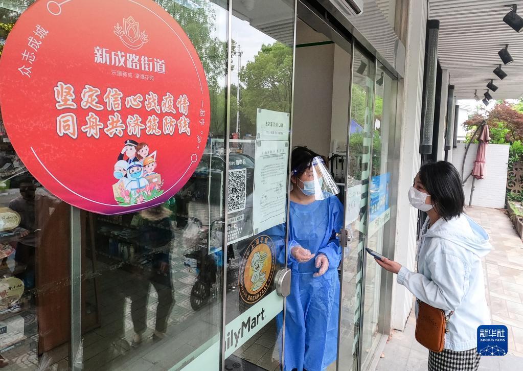 在上海市嘉定区新成路街道,一名顾客(右)在扫码后等待进入便利店(5月9日摄)。该街道经过认定符合防疫规范的经营场所会张贴红色圆形标识。