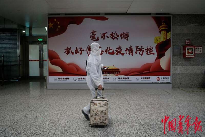 5月22日,上海地铁虹桥火车站站,一名身穿防护服的乘客刚刚抵达,他是当天第三波乘坐地铁抵达虹桥火车站的乘客。他身旁的墙上张贴着抗疫宣传海报:毫不松懈,抓好常态化疫情防控。中青报·中青网记者 李强/摄