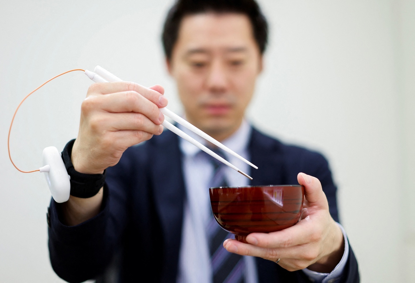 An employee of Kirin Holdings demonstrates chopsticks that can enchance food taste using an electrical stimulation waveform in Tokyo