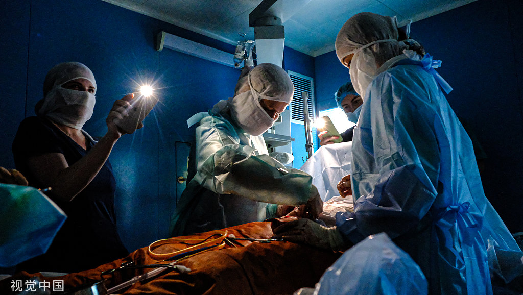 当地时间2022年11月30日，乌克兰基辅，停电后，医生用手机手电筒照明进行手术。