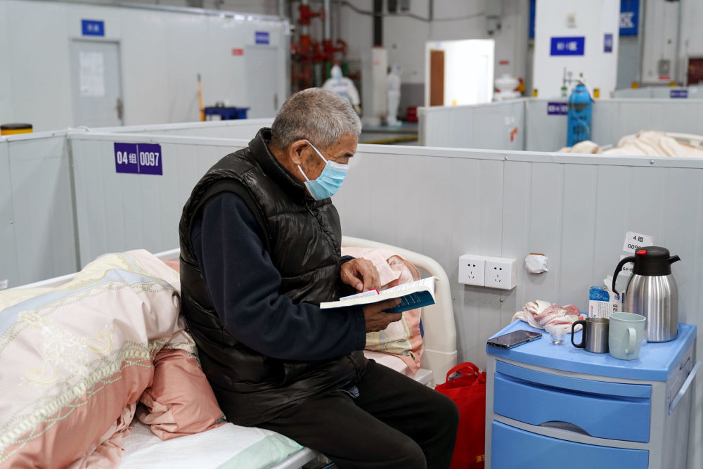 4月23日,在临港方舱医院,老年患者坐在床边看书