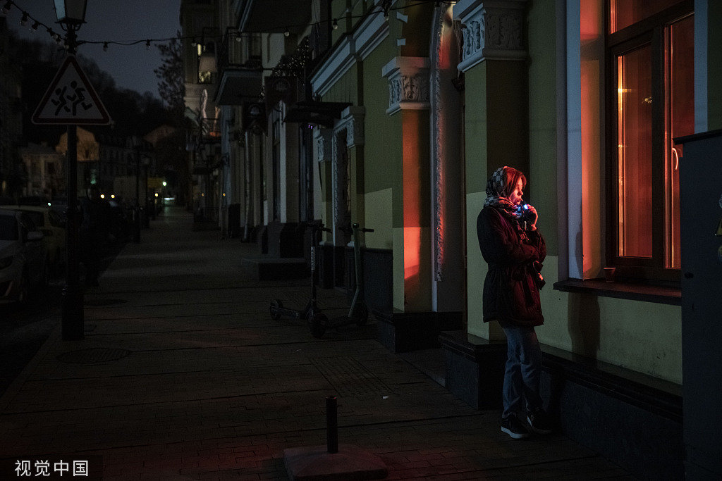 当地时间2022年11月7日，乌克兰基辅，一名妇女站在黑暗的街道上的一家咖啡馆外。