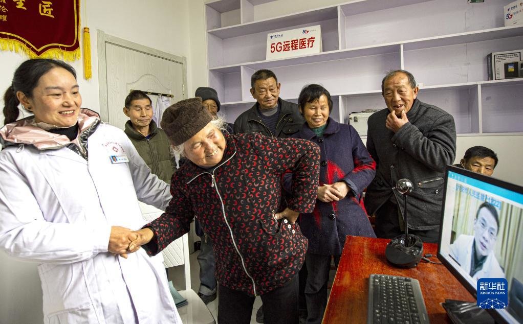 安徽省金寨县大湾村村民方临芳（前左二）指着自己身体疼痛的部位，在村医袁玲（左一）的帮助下向5G远程医疗会诊的专家讲述病情（2020年12月3日摄）。新华社发（陈力 摄）
