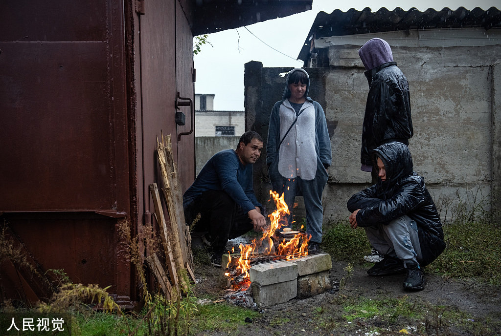 当地时间2022年10月20日，顿涅茨克地区，一个在公寓被毁后无家可归的家庭，离开他们现在居住的地下室后，围着火取暖。
