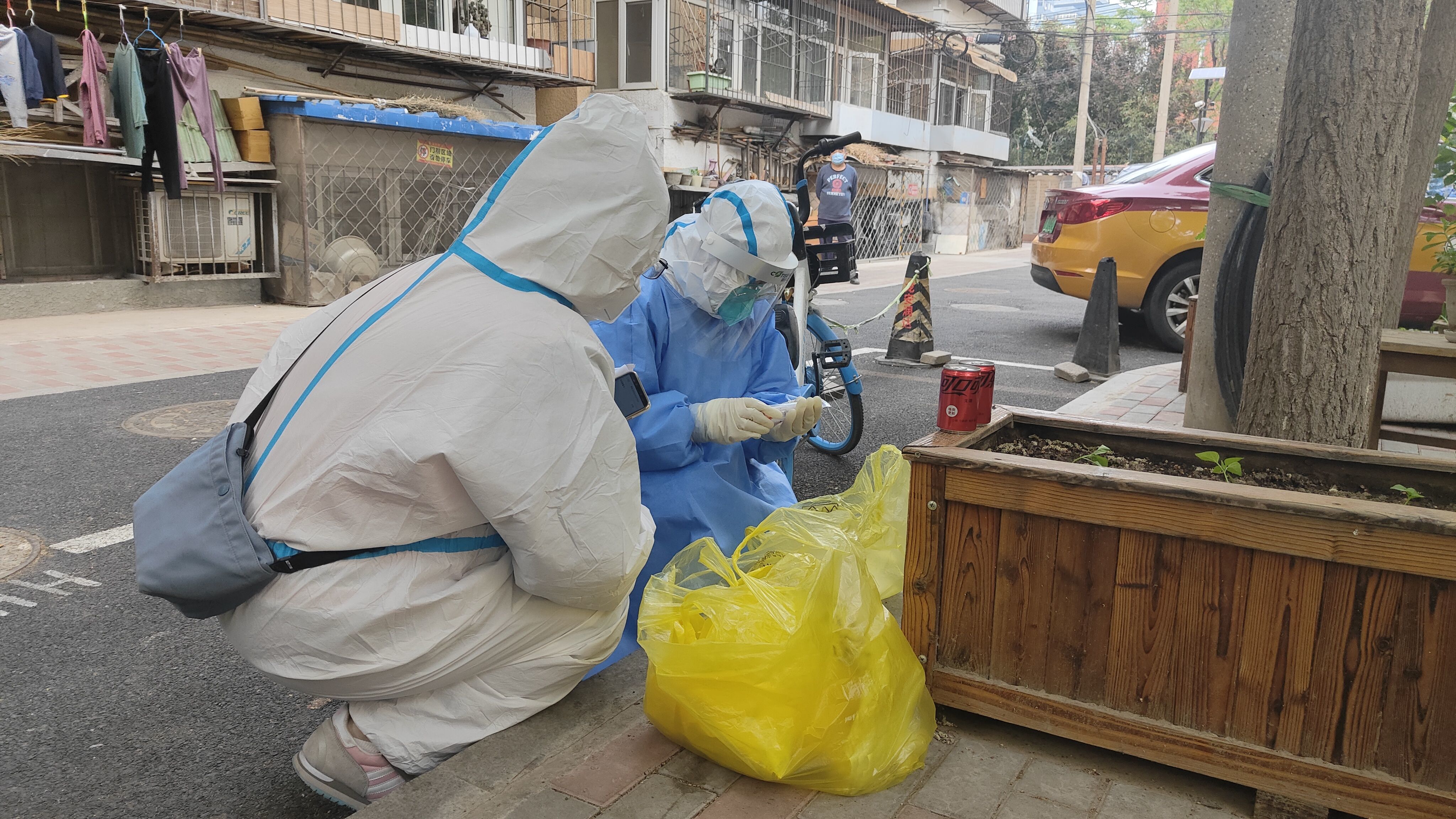 ▲4月29日下午,松五小区内,两名“大白”正在整理核酸样本,居民送来的两罐可乐一直摆在旁边。新京报记者 刘瑞明 摄