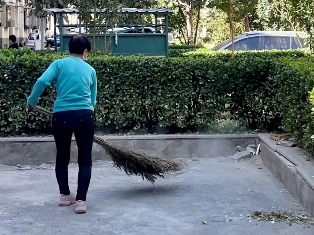 何明英在扫地,扫帚扬起一片尘土。摄影/郑可书