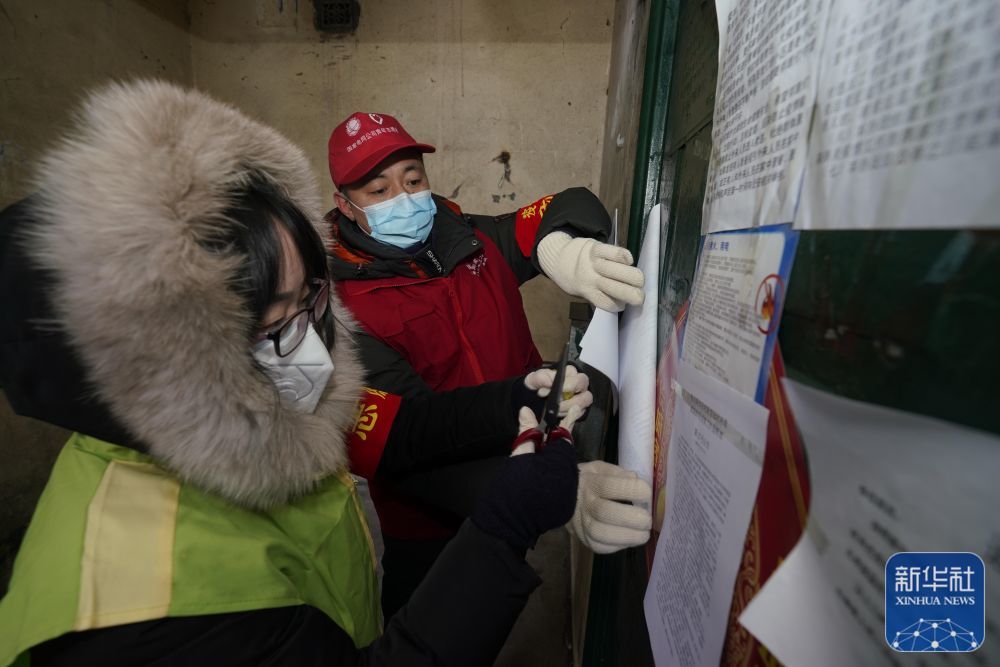 2020年2月14日,担任防疫志愿者的梅宏刚(右)在哈尔滨市一社区内粘贴防疫公告。新华社发(受访者供图)