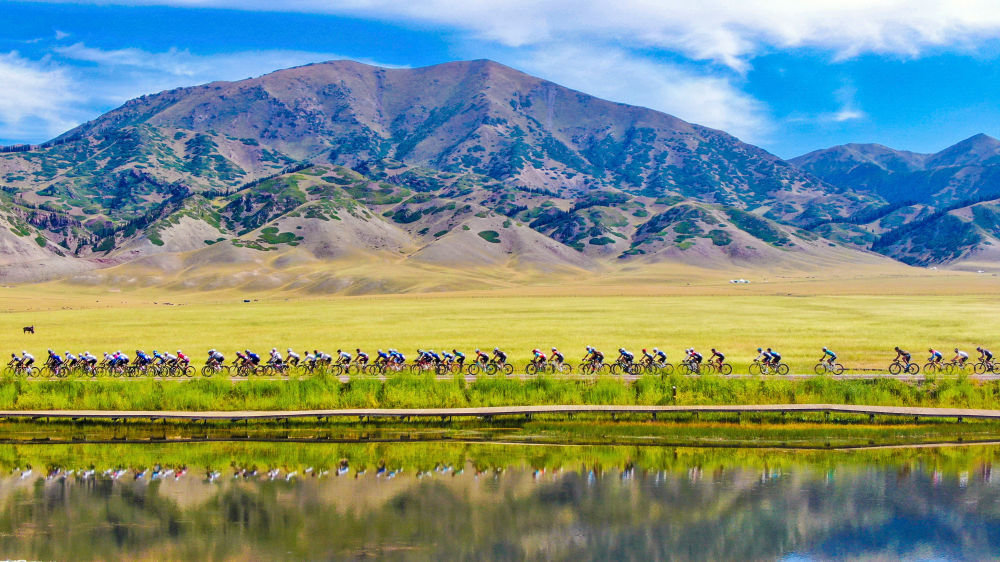 自行车赛选手在新疆赛里木湖国家湿地公园骑行(2022年7月26日摄,无人机照片)。新华社发(于苏甫·艾尼 摄)