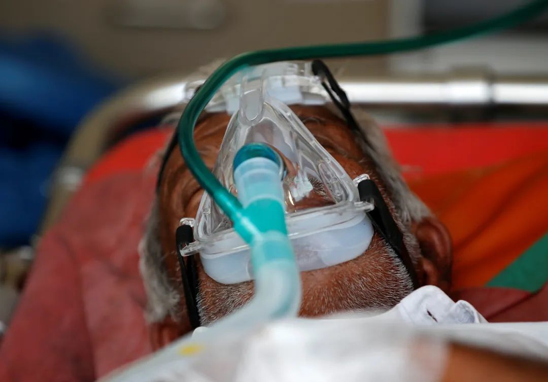 当地时间2021年4月25日，印度艾哈迈达巴德，一名新冠患者戴着氧气面罩，在救护车里等待进入医院治疗。图/IC photo