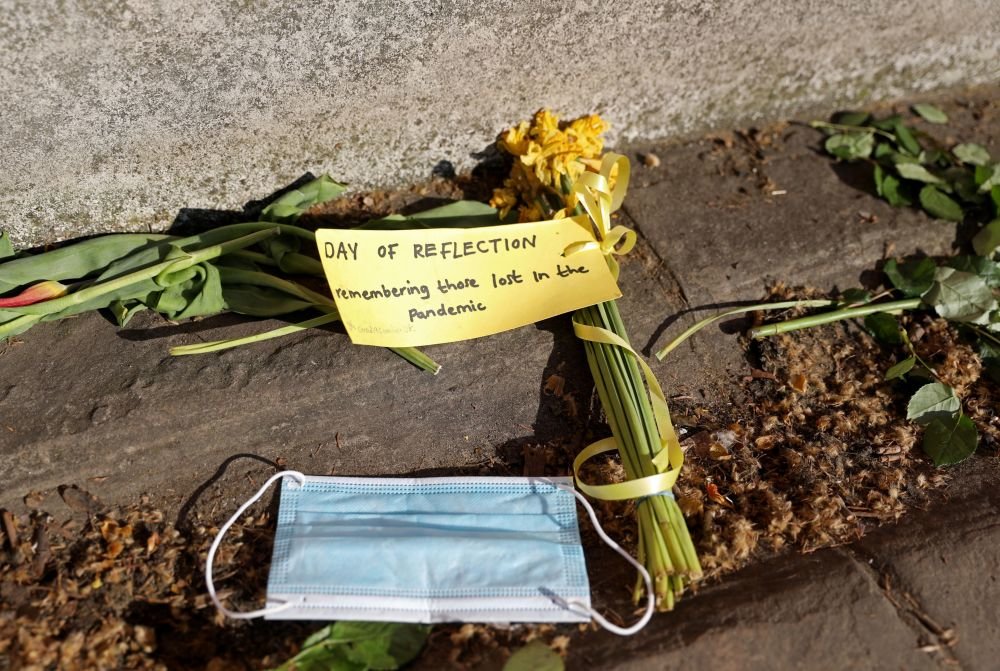 这是2022年3月27日在英国伦敦国家新冠纪念墙边拍摄的花束和口罩。花束旁的字条上写着“纪念在疫情中失去生命的人们”。（新华社记者李颖摄）