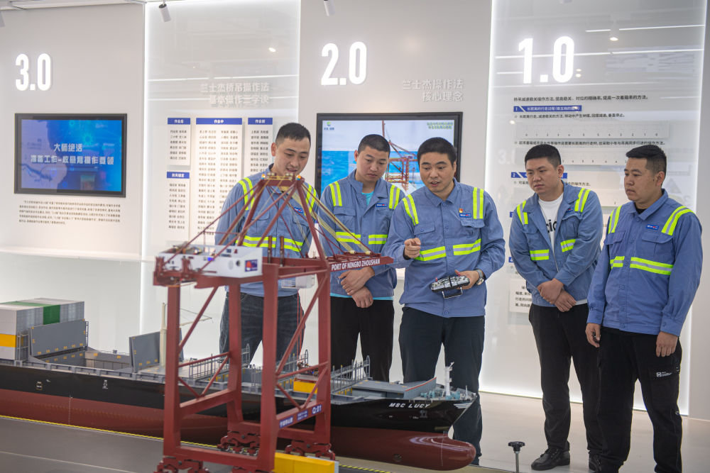 竺士杰（左三）在浙江宁波市北仑区穿山港区的工作室内利用模型向青年工人讲述桥吊操作原理（2022年5月24日摄）。新华社记者 江汉 摄