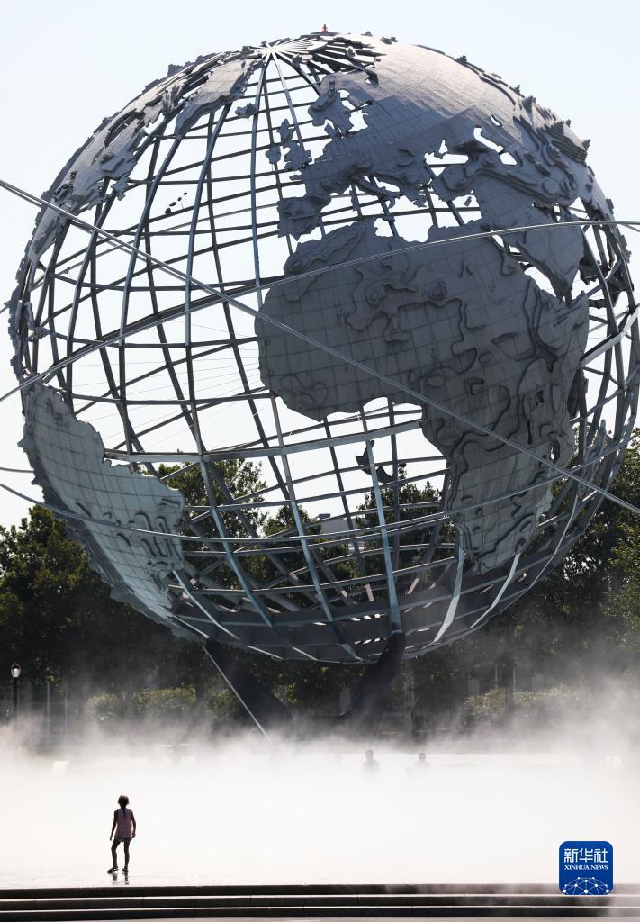 2021年8月13日，一名兒童冒著高溫天氣站在美國紐約科羅納公園水霧廣場的地球模型前。新華社記者 王迎 攝