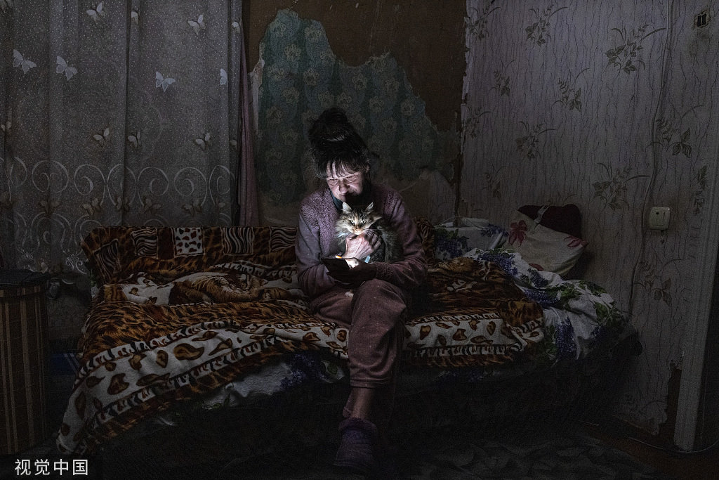 当地时间2022年10月20日，乌克兰博罗江卡，61岁的Tetyana Safonova和她的猫Asya坐在一起，看着她的手机。因为突然之间的停电，Tetyana没有准备好蜡烛。
