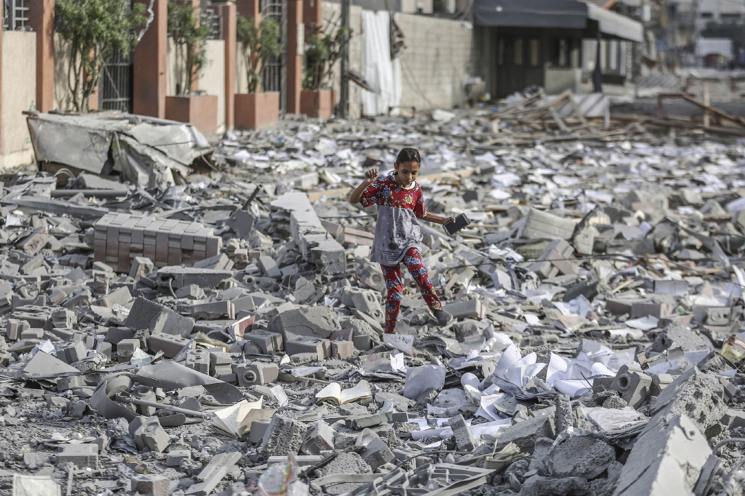 当地时间2023年10月10日，加沙地带，以色列空袭Rimal社区后，一名巴勒斯坦女孩走在被毁建筑的废墟中。视觉中国 图