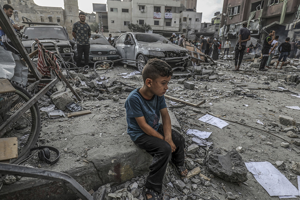 当地时间2023年10月10日，加沙地带汗尤尼斯，以色列发动空袭后，一名巴勒斯坦男孩坐在一栋被毁建筑的废墟中。