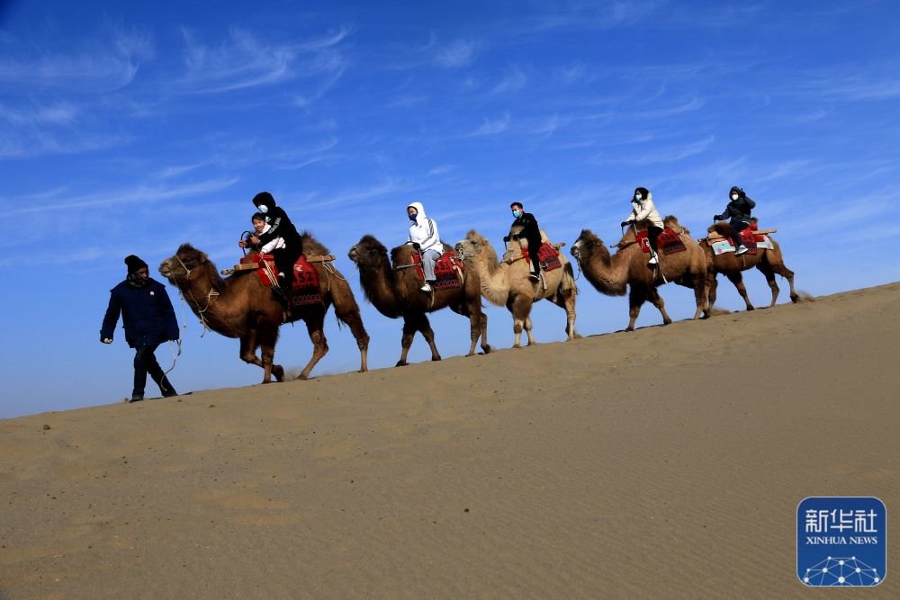 ↑1月27日，游客在甘肃省敦煌市鸣沙山月牙泉景区骑骆驼游览。新华社发（张晓亮 摄）