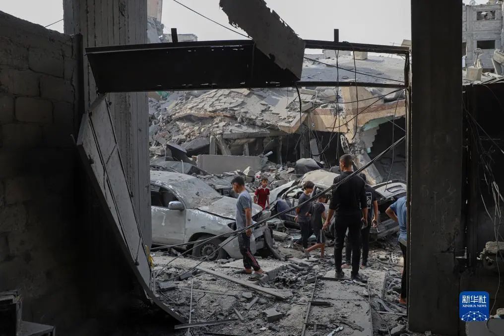 ▲10月9日，在加沙城，人们查看被以色列空袭炸毁的建筑废墟。（图源：新华社）