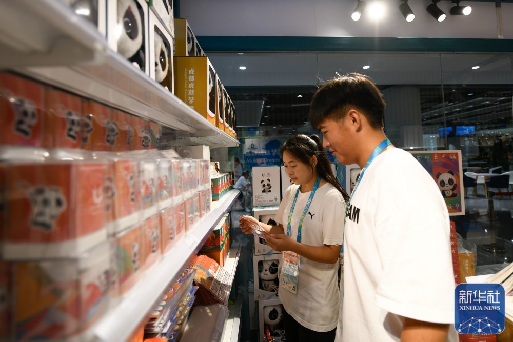 ↑7月14日,媒体工作人员在成都大运会主媒体中心大运会官方特许商品零售店内选购纪念品。新华社记者 胥冰洁 摄