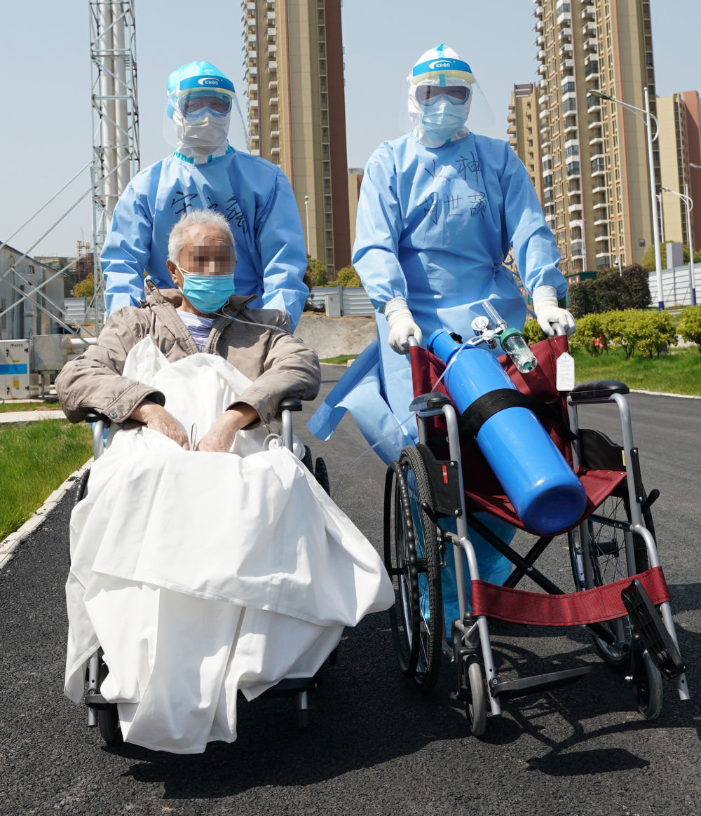 在湖北武汉，为确保患者有充足供氧，援鄂医生（右一）推着氧气瓶，护送81岁的新冠肺炎重症患者去做CT检查（2020年3月20日摄）。新华社记者 王毓国 摄