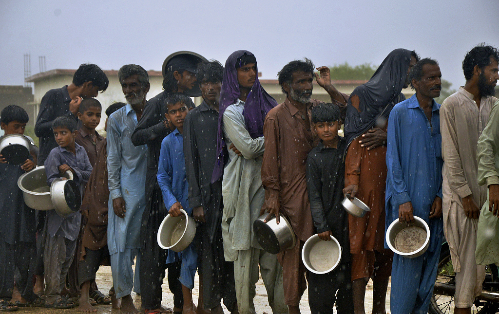 当地时间2023年6月15日，巴基斯坦信德省南部Sujawal，由于气旋风暴“比帕乔伊”的侵袭，人们在雨中排队等候志愿者分发的免费食物。
