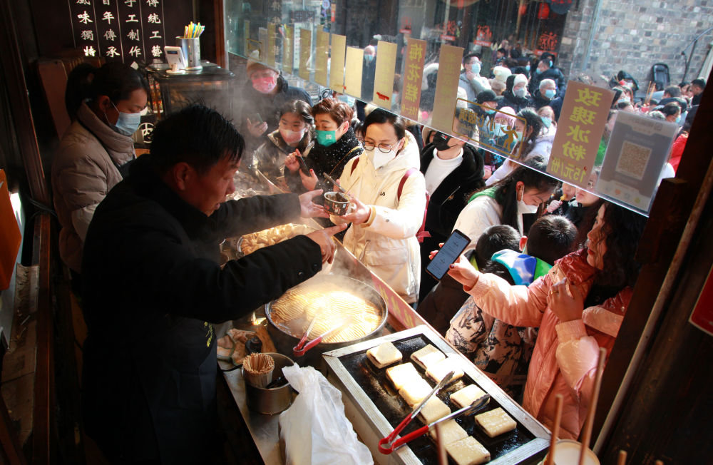 ↑1月24日，顾客在南京老门东的小吃摊位购买特色美食。新华社发（刘建华 摄）