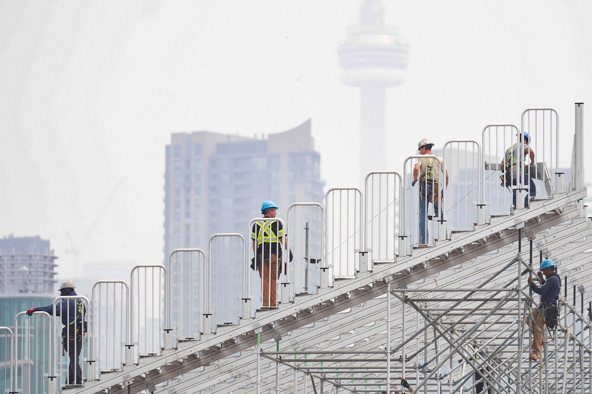 6月28日，加拿大多伦多，工人们正在为多伦多印地赛车大奖赛搭建临时看台，野火的烟雾掩盖了加拿大国家电视塔。