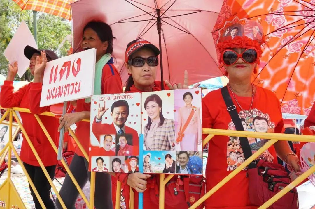 2014年5月10日，在泰国曼谷市郊，参加集会的红衫军成员举着印有泰国前总理他信和英拉照片的宣传板（杨云燕摄/本刊）