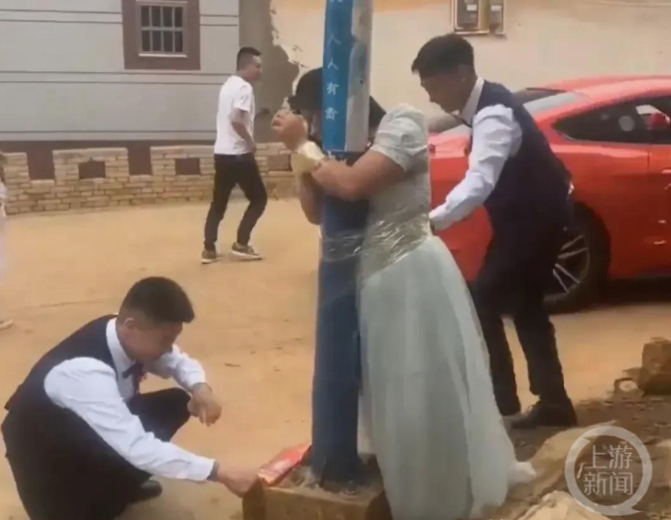 ▲伴郎将伴娘用胶带绑在电杆上,并点燃鞭炮。图片来源/视频截图