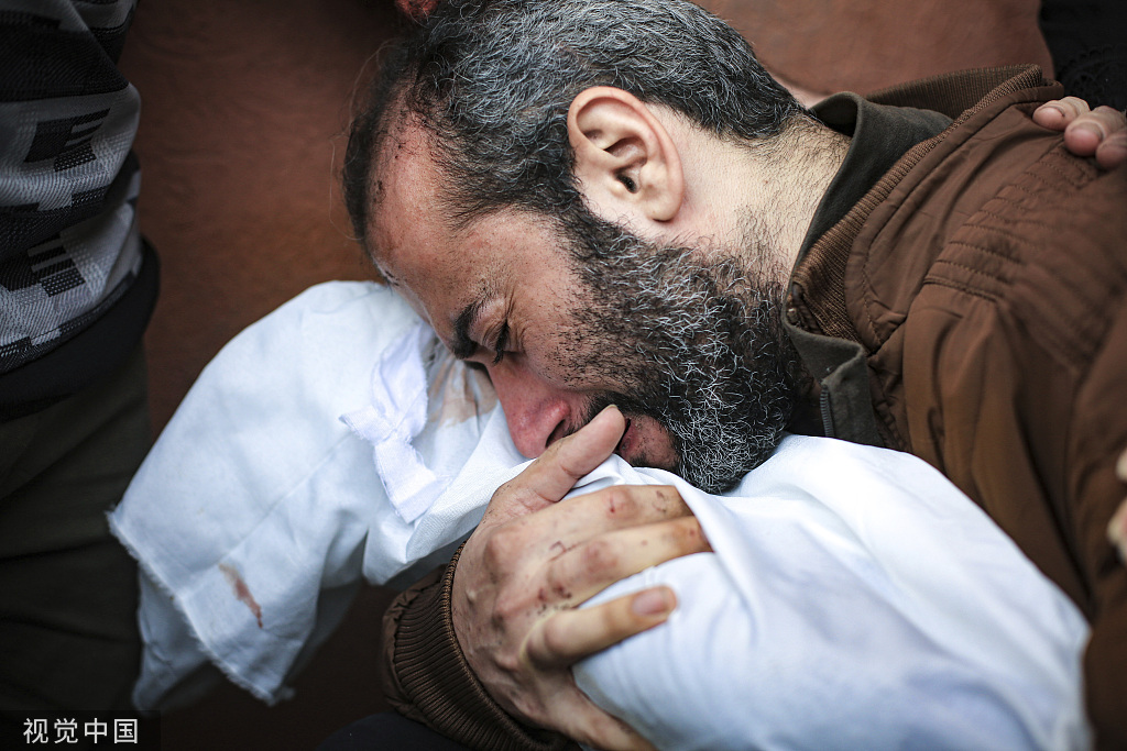 当地时间11月19日，加沙地带汗尤尼斯，一名男子抱着他在以色列轰炸中丧生的儿子的尸体。图片来源：视觉中国