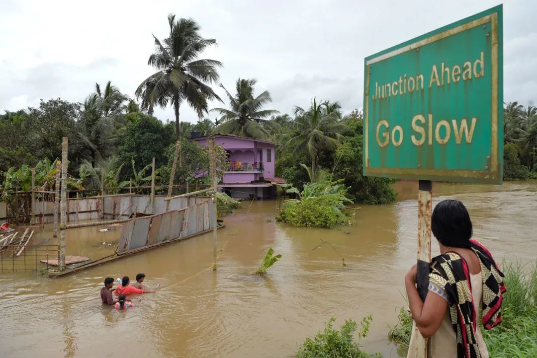 ◆2018年8月17日，在印度南部喀拉拉邦,一位印度妇女看着居民们趟过被洪水淹没的街道，旁边是被大水困住的房屋。