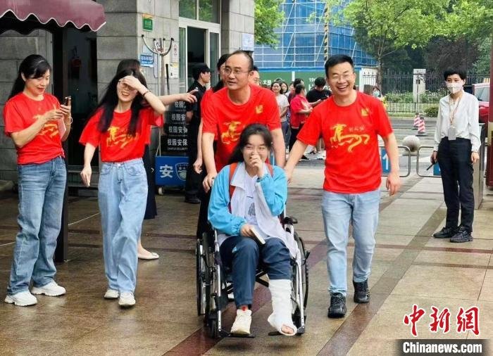 图为：高考首日，杭州源清中学教师陪伴腿脚不便的考生进入考场 源清中学供图
